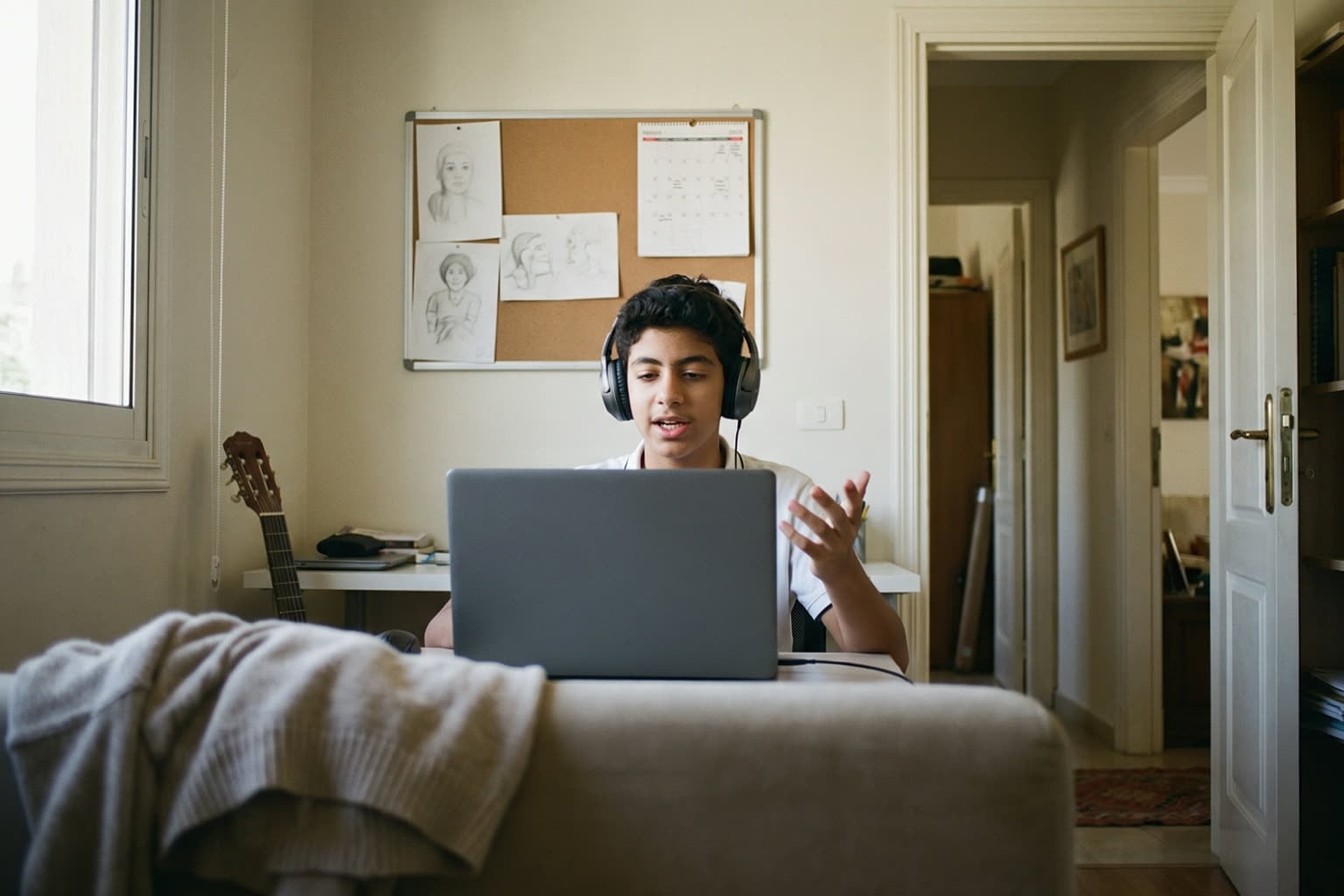 A teenage boy speaking English in a live class at the desk in his room